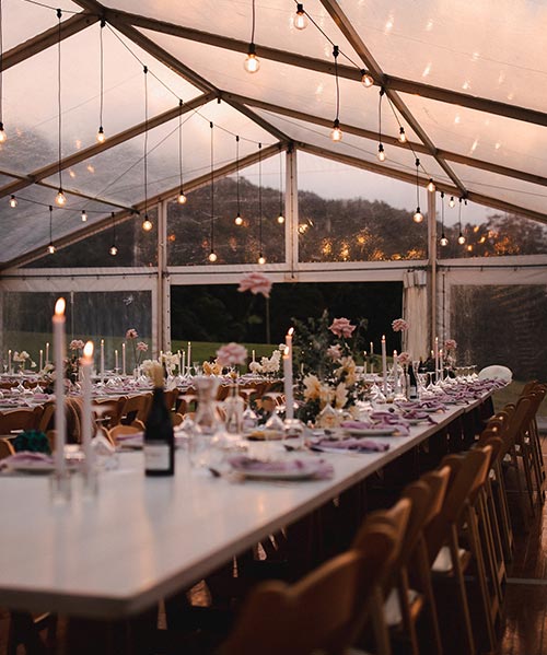 Laid table in wedding tent in evening with flowers and candles