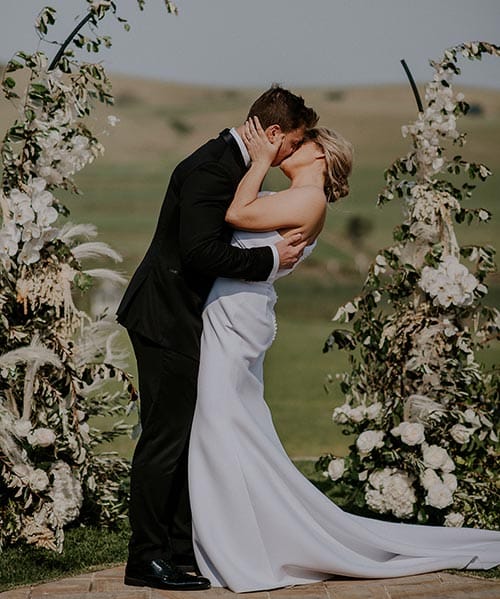Bride and Groom kissing between poles of flowers
